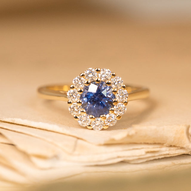 Bright blue sapphire and diamond cluster engagement ring featuring a vivid round sapphire surrounded by sparkling diamonds in yellow gold.