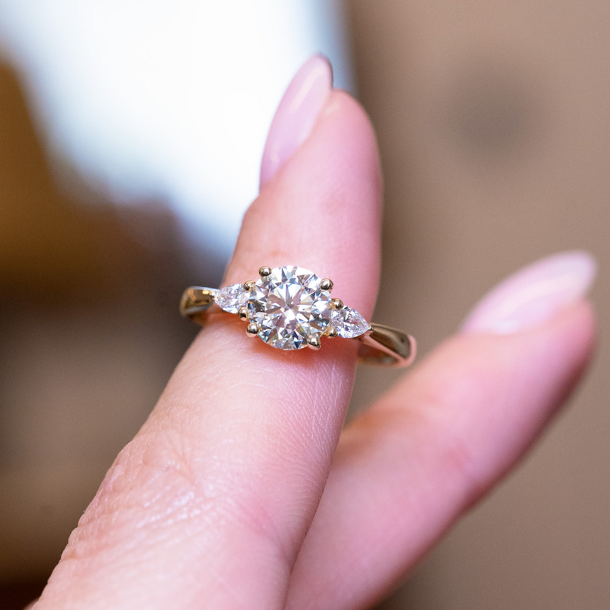Round brilliant-cut diamond three-stone engagement ring with central round diamond and balanced on a finger.