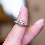 Round brilliant-cut diamond three-stone engagement ring with central round diamond and balanced on a finger.