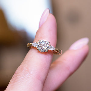 Round brilliant-cut diamond three-stone engagement ring with central round diamond and balanced on a finger.