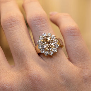 Close-up of a vintage fancy coloured brown diamond cluster cocktail ring on the finger, showcasing an oval brown diamond encircled by brilliant-cut diamonds.