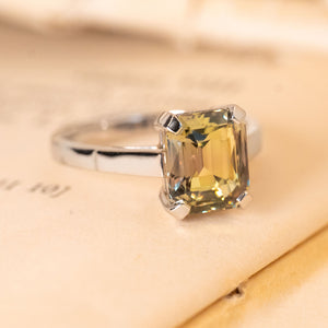 Emerald-cut colour-change sapphire solitaire ring displaying green and brown hues in a classic white gold engagement ring setting.