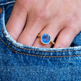 Blue sapphire ring worn on hand with denim pocket detail.