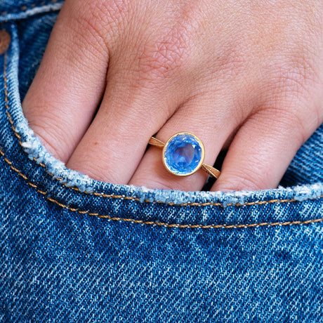Blue sapphire ring worn on hand with denim pocket detail.