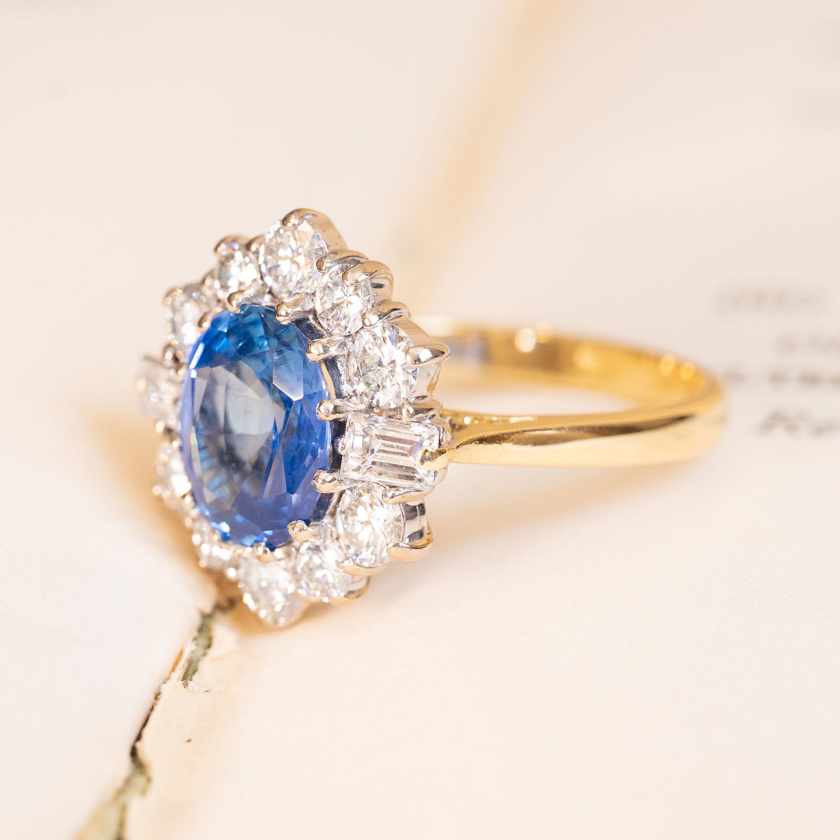 Vintage cornflower blue sapphire and diamond cluster ring with oval sapphire, diamond halo and baguette-cut diamond accents.