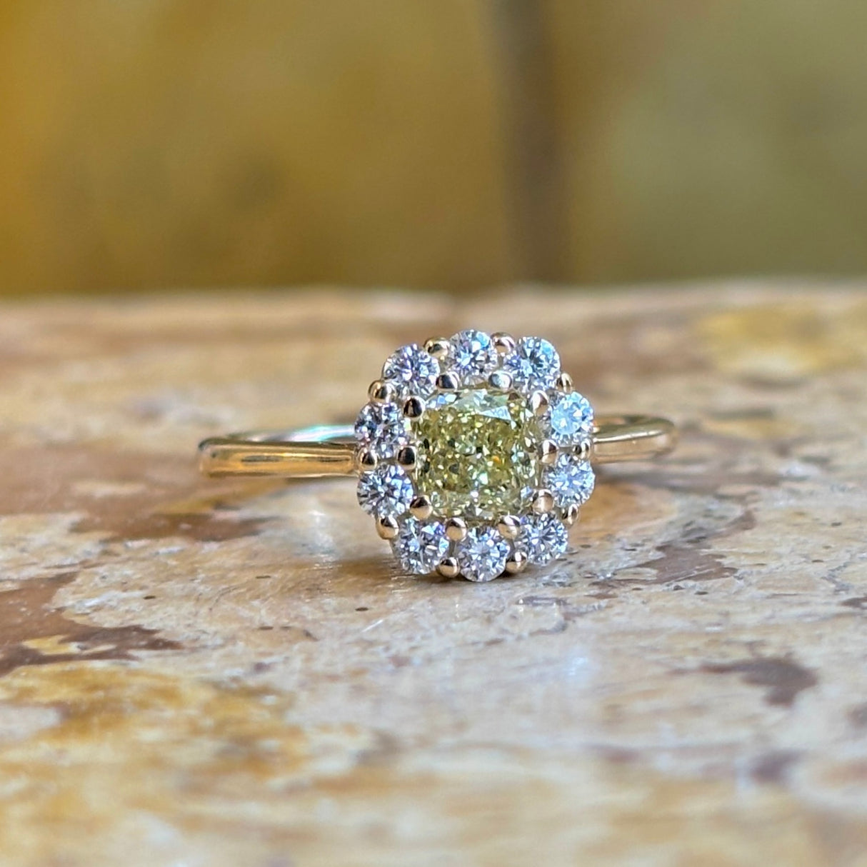 Cushion-cut fancy yellow diamond cluster ring surrounded by white diamonds in yellow gold.