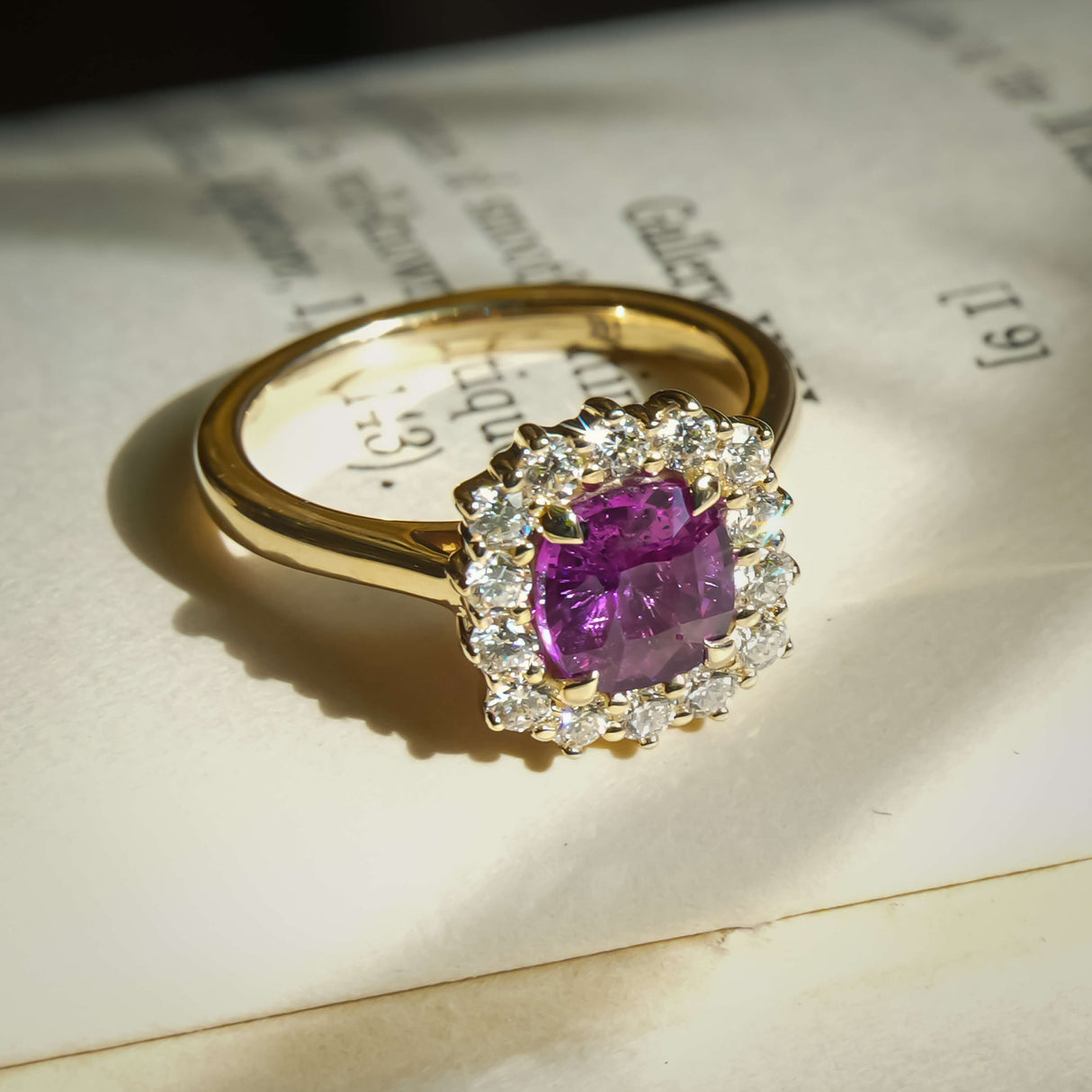Cushion cut pink sapphire and diamond cluster halo engagement ring in yellow gold setting