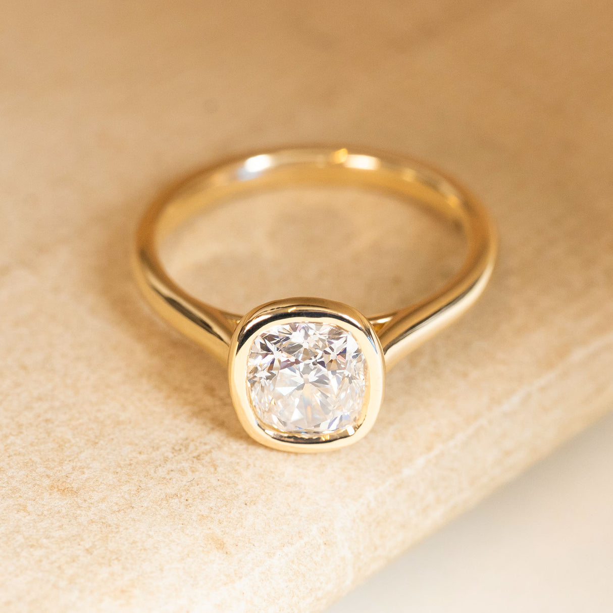 Cushion old-cut diamond solitaire engagement ring in yellow gold with a smooth rub-over setting.