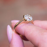Cushion old-mine cut diamond solitaire engagement ring with raised diamond setting held between fingers.