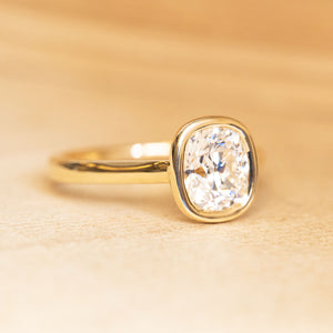 Cushion old-cut diamond solitaire engagement ring in a yellow gold rub-over setting.