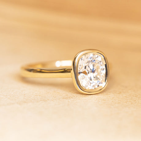 Cushion old-cut diamond solitaire engagement ring in a yellow gold rub-over setting.