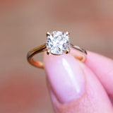 Cushion old-mine cut diamond solitaire engagement ring held between fingers with gold band.