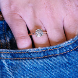 Cushion old-mine cut diamond solitaire engagement ring worn on hand with denim pocket styling.