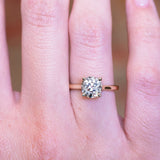 Cushion old-mine cut diamond solitaire engagement ring with claw-set diamond worn on finger.