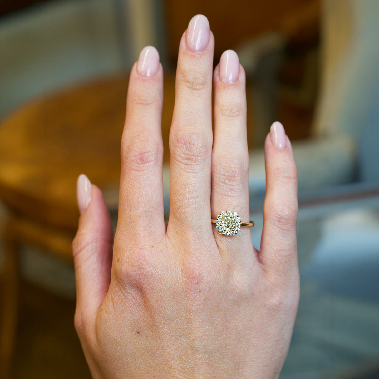Diamond cluster engagement ring worn on hand with round brilliant centre diamond and halo setting.