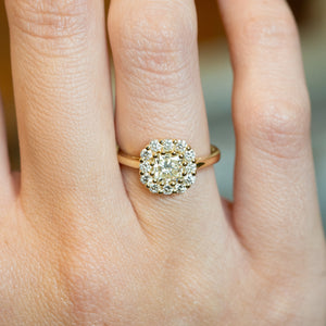 Diamond cluster engagement ring worn on finger with brilliant-cut diamond halo and yellow gold band.