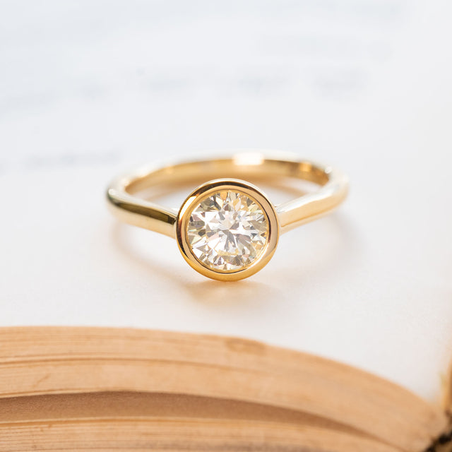 Diamond rub-over solitaire engagement ring with round brilliant-cut diamond in yellow gold.