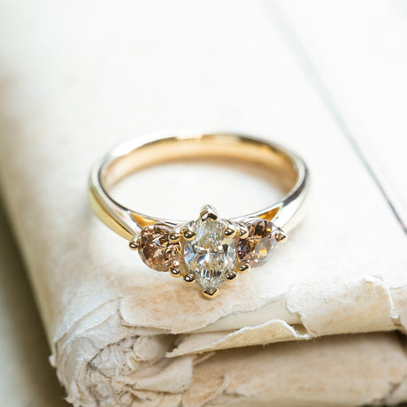 Diamond three-stone engagement ring with marquise-cut centre diamond resting on antique books.