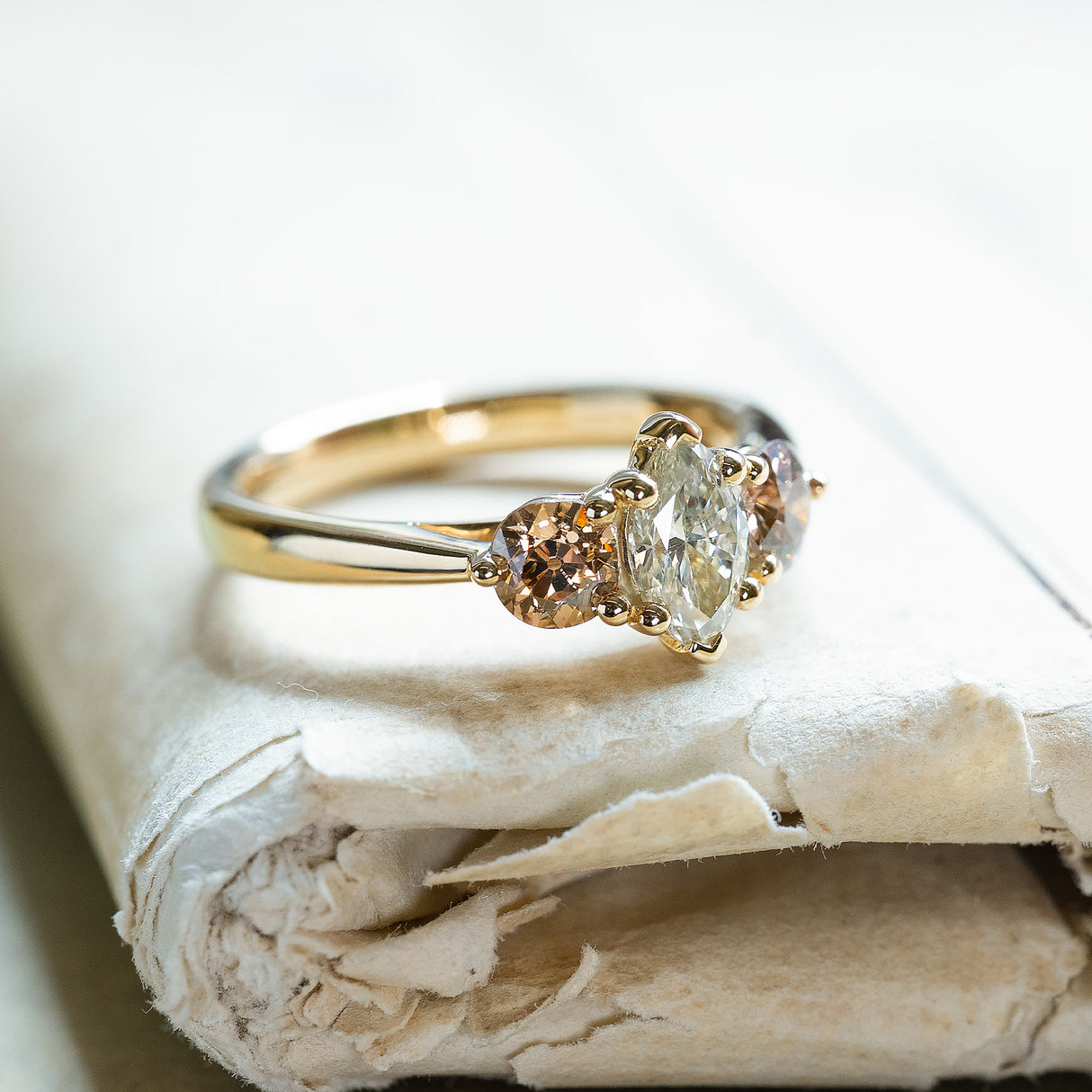 Diamond three-stone engagement ring with marquise centre diamond and warm-toned side diamonds on gold band.