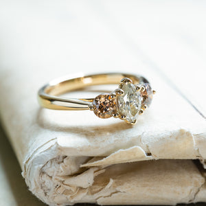 Diamond three-stone engagement ring with marquise centre diamond and warm-toned side diamonds on gold band.