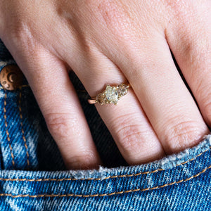 Diamond three-stone engagement ring worn on hand with denim pocket styling.