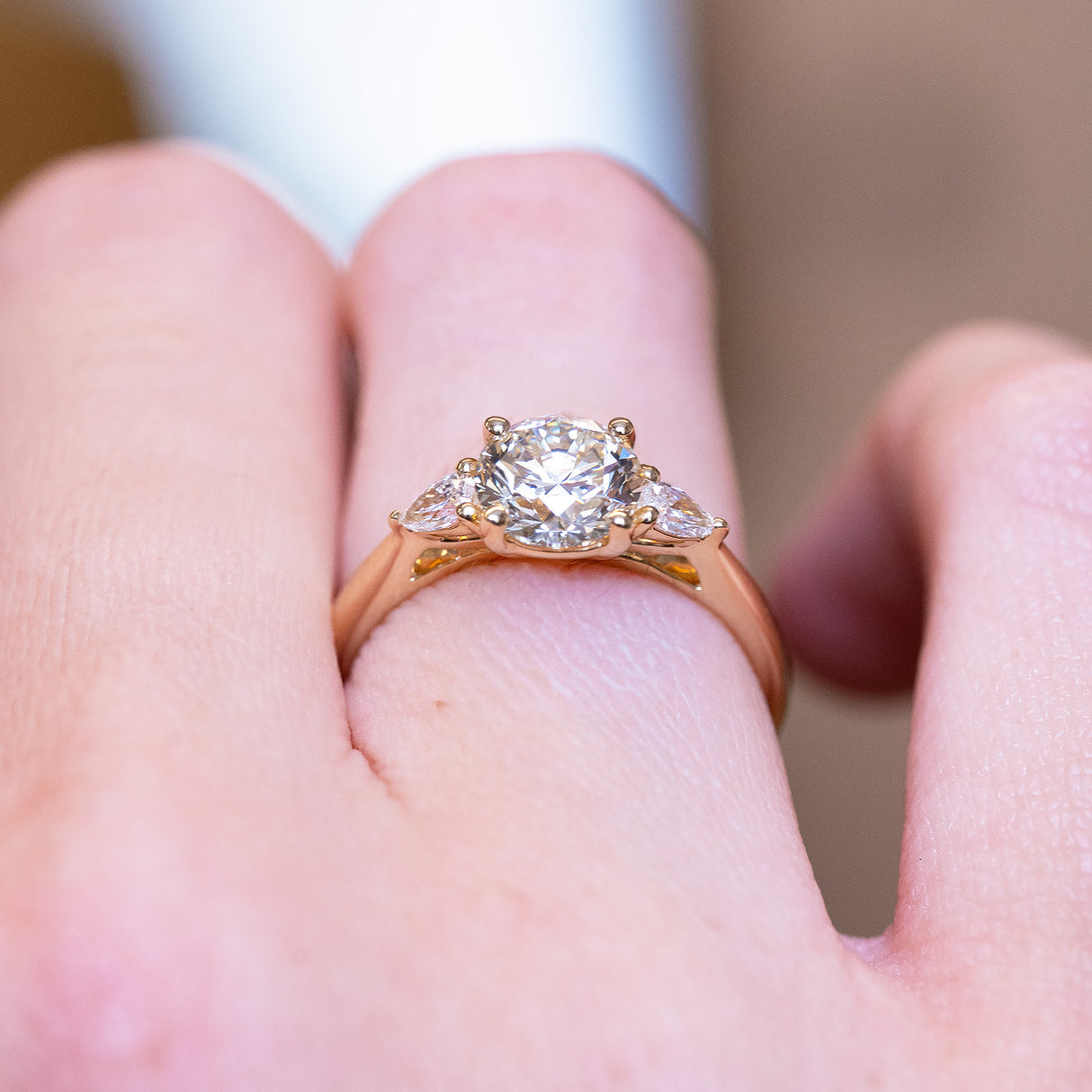 Round brilliant-cut diamond three-stone engagement ring with polished gold band and diamond side stones.