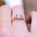 Round brilliant-cut diamond three-stone engagement ring with polished gold band and diamond side stones.