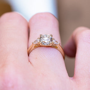 Round brilliant-cut diamond three-stone engagement ring with polished gold band and diamond side stones.