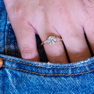 Round brilliant-cut diamond three-stone engagement ring worn on hand with denim pocket styling.