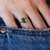 Close-up of a hand wearing an emerald ring on blue denim fabric.