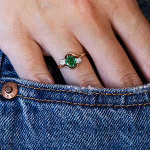 Close-up of a hand wearing an emerald ring on blue denim fabric.