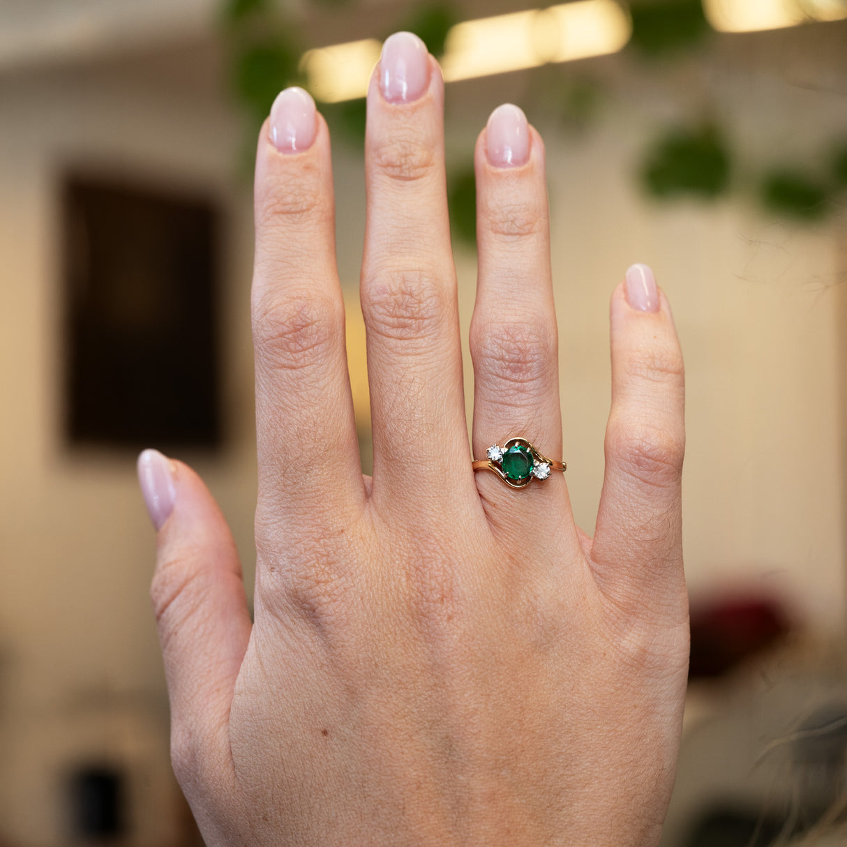 Emerald and diamond three stone ring worn on hand with natural manicure.