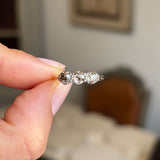Antique Edwardian three-stone ring in yellow gold featuring old-cut brown, pink and champagne coloured diamonds, held between fingers against a softly blurred vintage interior background.