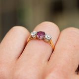 Gold ring with a central ruby and two diamonds on a finger against a blurred background.