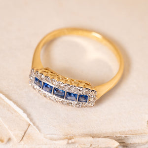 Antique Edwardian sapphire and diamond cluster ring with a row of square-cut blue sapphires surrounded by old-cut diamonds in yellow gold.