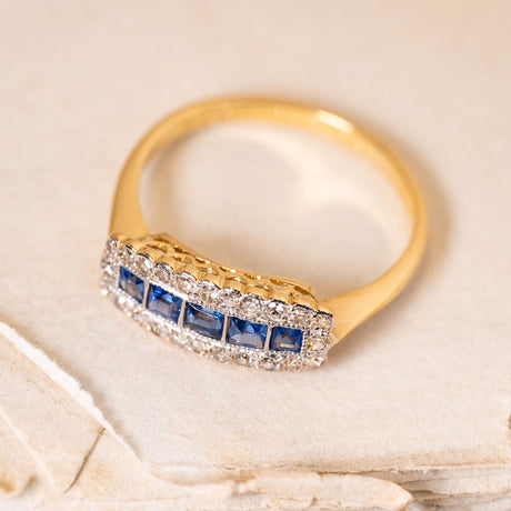 Antique Edwardian sapphire and diamond cluster ring with a row of square-cut blue sapphires surrounded by old-cut diamonds in yellow gold.