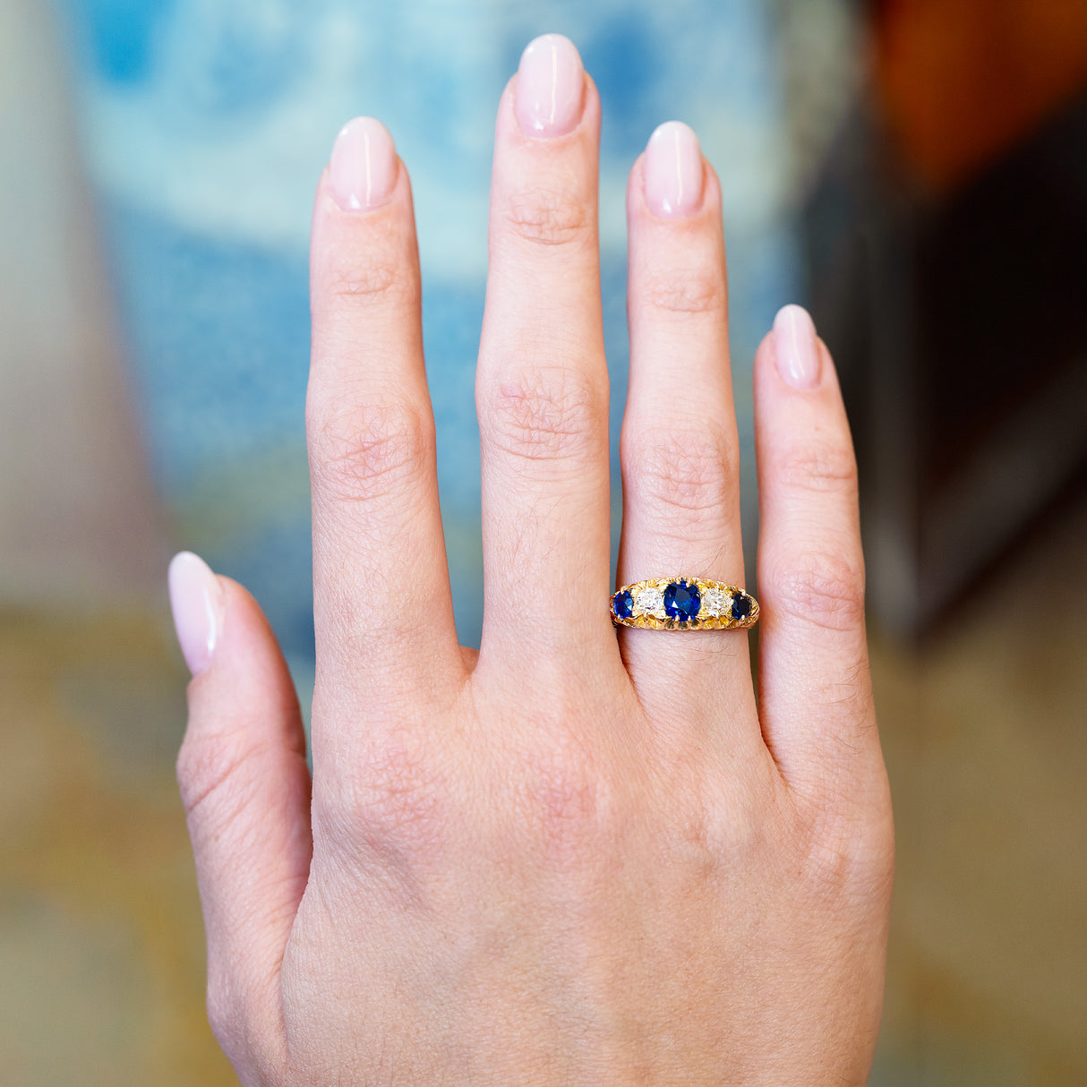 Antique five stone ring worn on hand with blue sapphire and old mine cut diamonds.