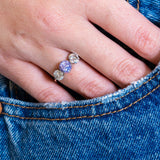 Close-up of a hand wearing a three-stone ring with a sapphire, set against a blue denim background.