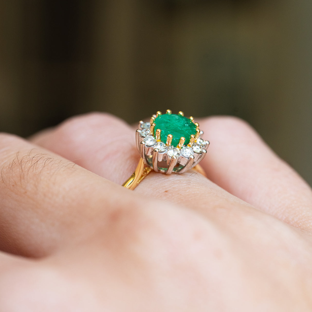 Emerald cluster ring detail highlighting raised setting and surrounding diamonds.