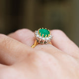 Emerald cluster ring detail highlighting raised setting and surrounding diamonds.
