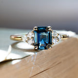 Emerald cut blue sapphire three stone ring with diamond sides on book.