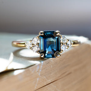 Emerald cut blue sapphire three stone ring with diamond sides on book.
