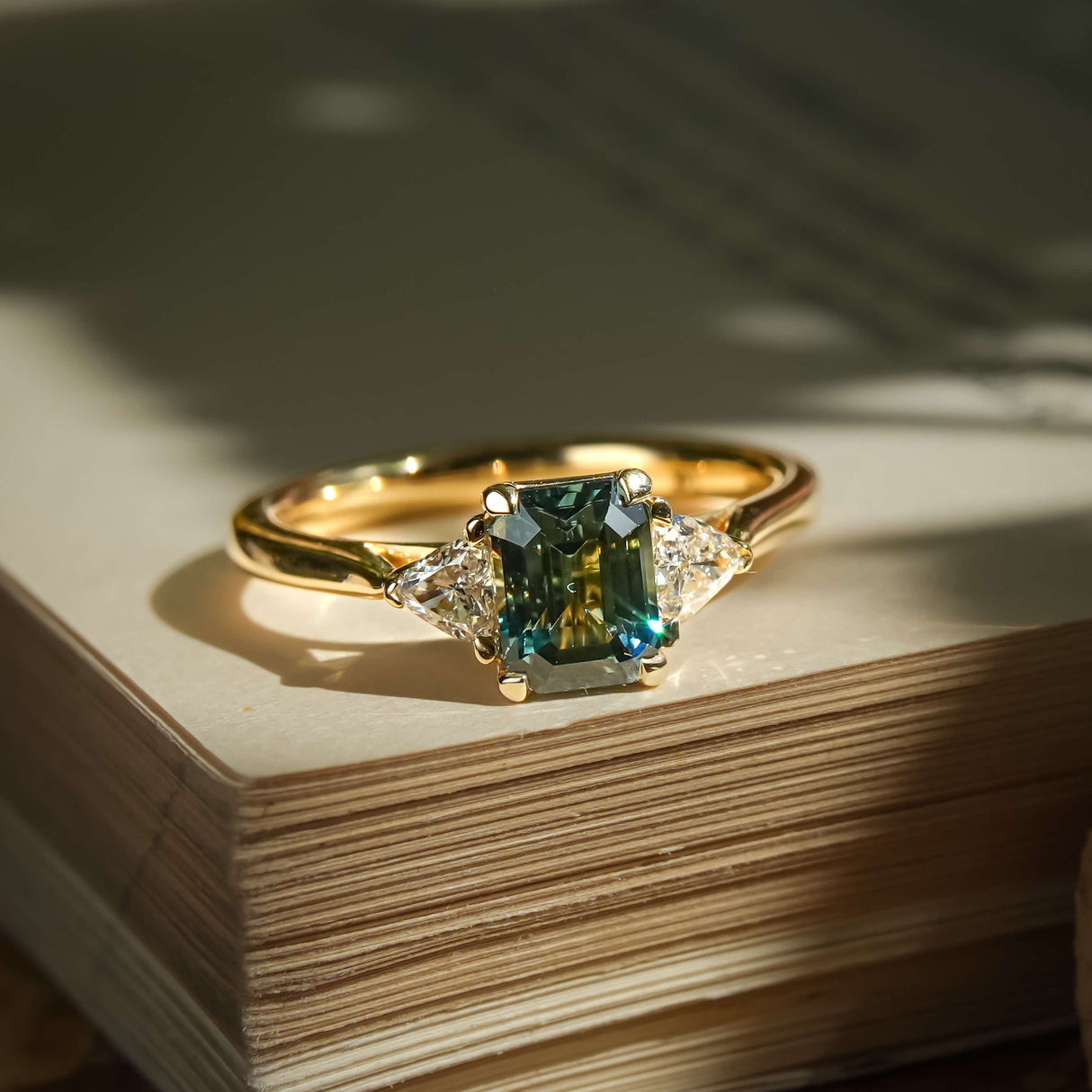Emerald cut green sapphire and diamond three stone engagement ring in yellow gold band
