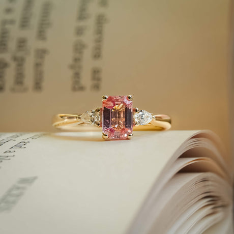 Emerald cut pink sapphire with diamond three stone engagement ring in yellow gold