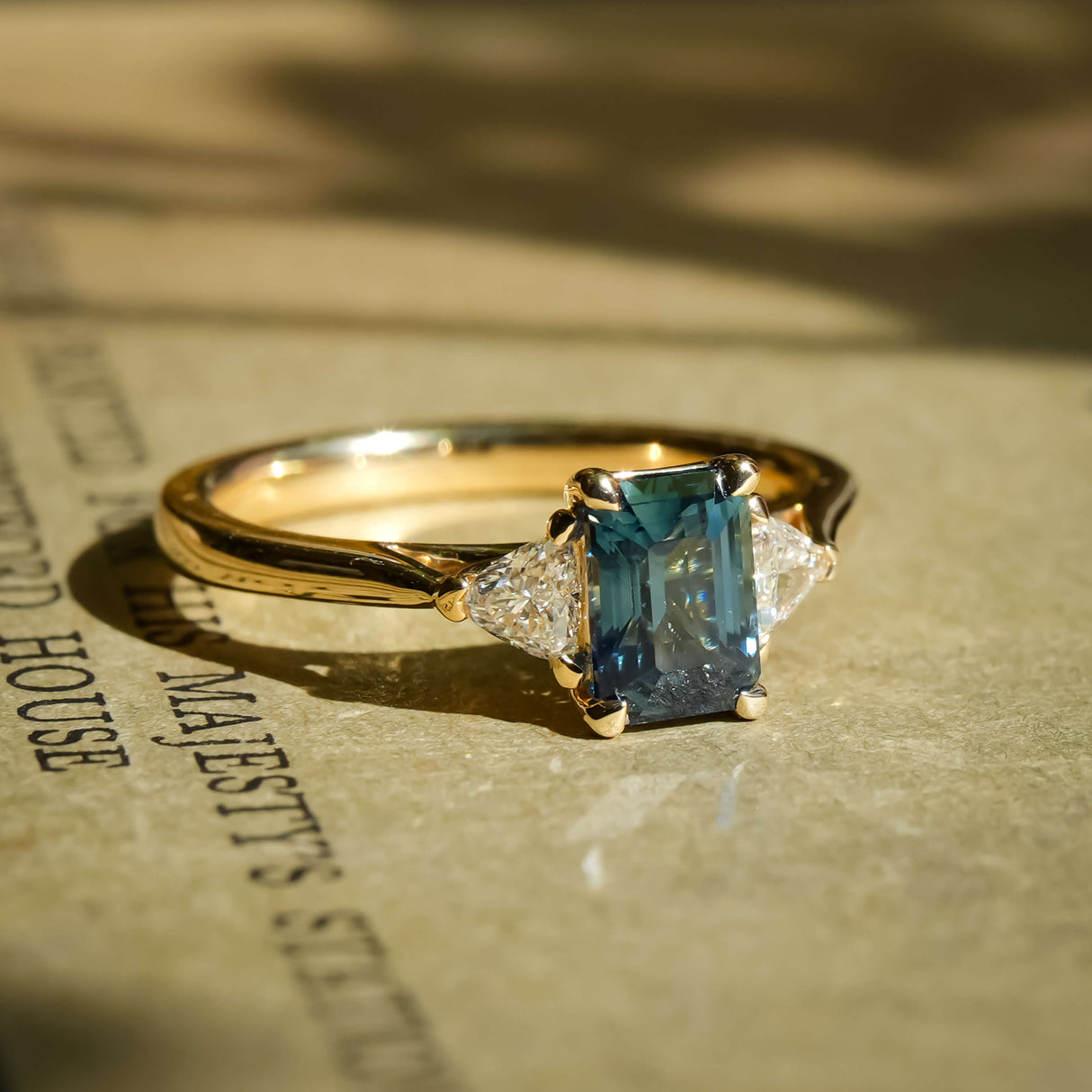Emerald cut teal sapphire with diamond three stone engagement ring in yellow gold