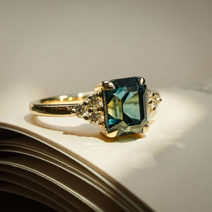 Emerald cut teal sapphire engagement ring with diamond trefoil cluster setting