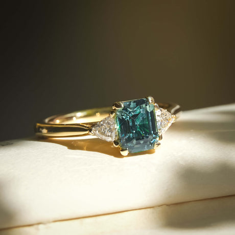 Emerald cut teal sapphire and diamond three stone engagement ring in yellow gold band