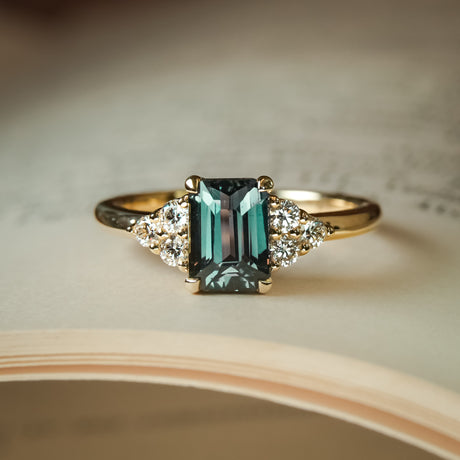 Emerald cut teal sapphire engagement ring with trefoil diamond cluster