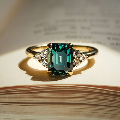 Emerald cut teal sapphire ring with diamond trefoil cluster setting