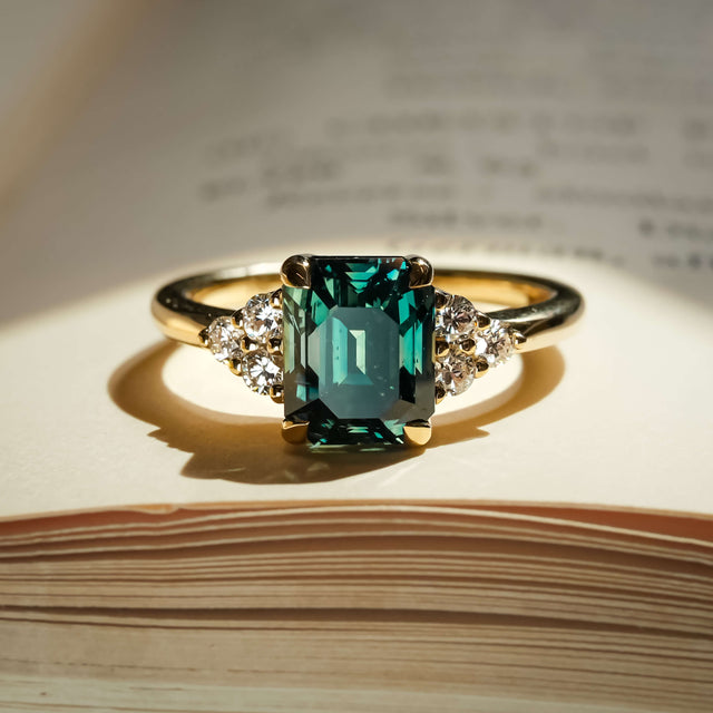 Emerald cut teal sapphire ring with diamond trefoil cluster setting